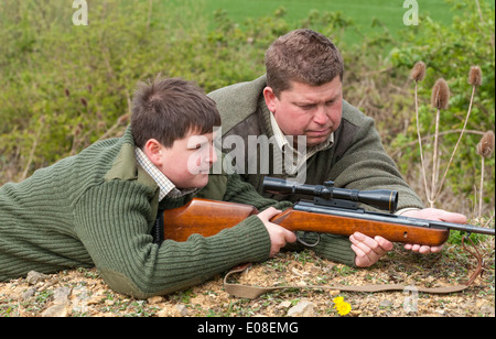 Ein kleiner Junge mit einem Luftgewehr im Zielschießen von seinem Vater trainiert wird Stockfoto
