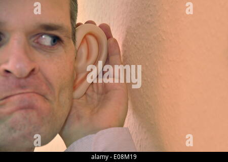 Illustration - Ein Mann mit riesigen Gummi-Ohren spioniert an einer Wand in Deutschland, 27. Februar 2011. Fotoarchiv für Zeitgeschichte - KEIN KABELDIENST Stockfoto