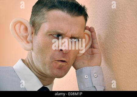 Illustration - Ein Mann mit riesigen Gummi-Ohren spioniert an einer Wand in Deutschland, 27. Februar 2011. Fotoarchiv für Zeitgeschichte - KEIN KABELDIENST Stockfoto