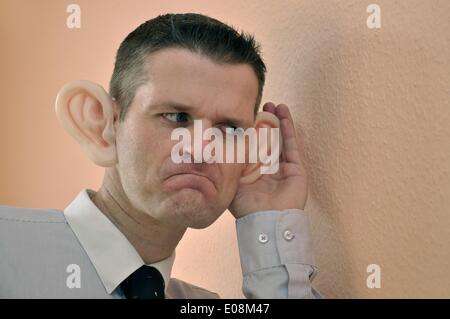 Illustration - Ein Mann mit riesigen Gummi-Ohren spioniert an einer Wand in Deutschland, 27. Februar 2011. Fotoarchiv für Zeitgeschichte - KEIN KABELDIENST Stockfoto