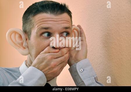 Illustration - Ein Mann mit riesigen Gummi-Ohren spioniert an einer Wand in Deutschland, 27. Februar 2011. Fotoarchiv für Zeitgeschichte - KEIN KABELDIENST Stockfoto