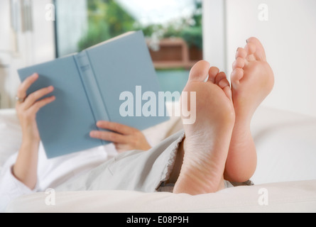 Frau liegend mit den Beinen erhöht auf einer Couch und ein Buch zu lesen. Stockfoto