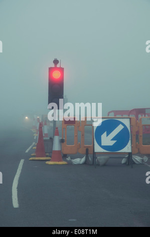 UK NEBLIGEN STRAßE MIT TEMPORÄREN ROTE AMPEL FÜR BAUSTELLEN Stockfoto