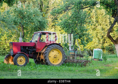 rustikale alte Ackerschlepper mit gelben Rädern und Harow in Gartengras Stockfoto