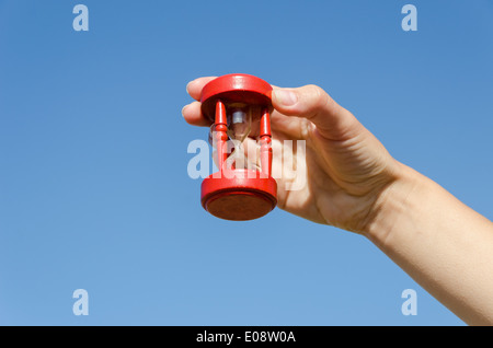 rot aus Holz alte Sanduhr in weiblicher Hand am blauen Himmelshintergrund Stockfoto