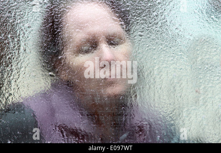 Der lange Winter - Bild einer einzigen, traurig aussehende Frau durch ein starkes Blatt des Eises Stockfoto