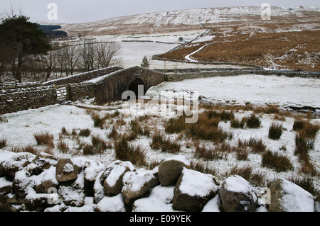 Widdale Beck fließt durch schneebedeckte Felder und unter eine Steinbrücke mit der Grat des Widdale fiel hinter. Stockfoto