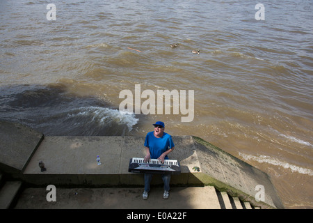 Straßenmusiker spielen eine elektronische Orgel singen am Flussufer. Diese als Straßenmusikant regelmäßig singt alte klassische pop-Songs und engagiert sich immer sein Publikum mit seinen Cockney Geplänkel auf der Southbank. South Bank ist eine bedeutende Kunst- und Unterhaltungsviertel, es ist voll mit Besuchern und Touristen am Flussufer Gehweg. London, UK. Stockfoto