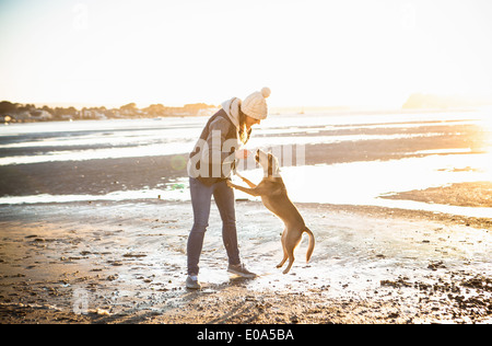 Junge Frau spielt mit ihrem Hund am Strand Stockfoto