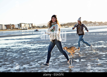 Zwei Freundinnen, die laufen mit Hund am Strand Stockfoto