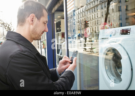 Mitte erwachsener Mann Auschecken Waschmaschine im Shop mit smartphone Stockfoto