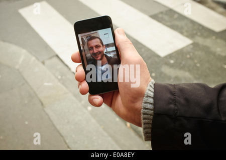 Mitte erwachsenen Mannes auf Bürgersteig halten Smartphone mit Foto auf dem Bildschirm Stockfoto