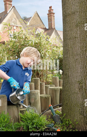 Schuljunge Pflanzen im Garten gießen Stockfoto