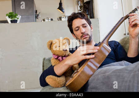 Mitte erwachsener Mann liegend auf Sofa, Gitarre spielen Stockfoto