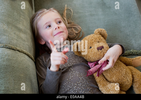 Junges Mädchen auf Sofa liegend mit ihr Teddy Bär Stockfoto