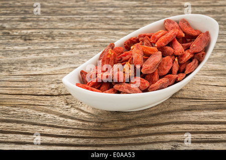 getrocknete Goji-Beeren in eine kleine Keramikschale gegen gemaserte Holz Stockfoto