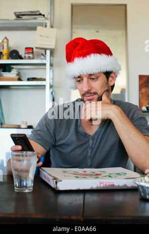 Porträt von Mitte erwachsenen Mann trägt Weihnachtsmütze Blick auf Handy Stockfoto