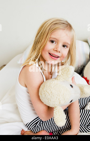 Porträt des jungen Mädchens kniend auf dem Bett mit Stofftier Stockfoto