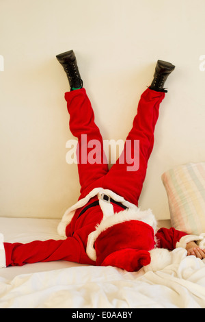Kleiner Junge verkleidet als Weihnachtsmann auf Bett mit Beine angehoben Stockfoto