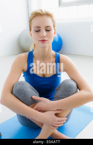 Junge Frau sitzt auf Gymnastikmatte, Augen geschlossen Stockfoto