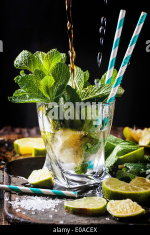 Glas Mojito cocktail mit strömenden Rum und Soda, frische Minze, Limetten und Eiswürfel auf schwarzem Hintergrund. Stockfoto