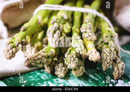 Nahaufnahme von Haufen junger Grüner Spargel mit Meersalz über grüne Holztisch. Stockfoto