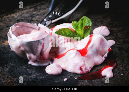 Nahaufnahme von Schmelzen Erdbeereis mit frischer Minze und Metalllöffel in schwarzen Tisch. Stockfoto