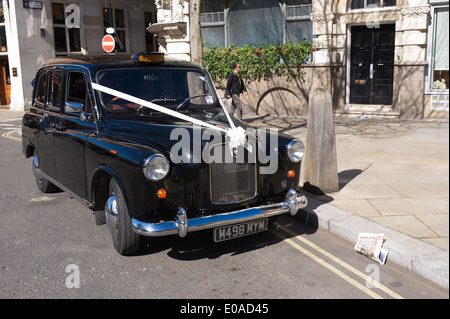 Schwarzes Taxi Taxi in London als Hochzeitsauto, mit einem weißen Bogen und Band auf der Fronthaube verwendet wird. Stockfoto