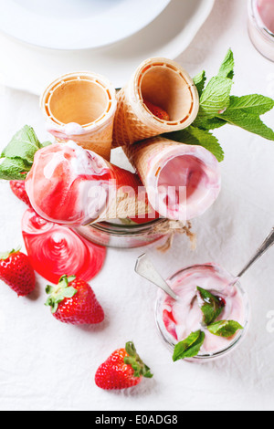 Wafer-Kegel mit Erdbeer Eis mit Sirup, Minze und frischen Erdbeeren serviert in Glas über weiße Textilien. Ansicht von oben. Stockfoto