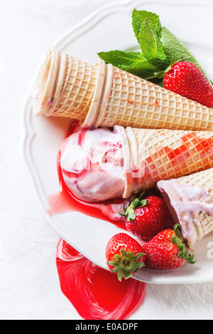 Wafer-Kegel mit Erdbeer Eis mit Sirup, Minze und frische Erdbeeren auf weißem Teller serviert. Stockfoto