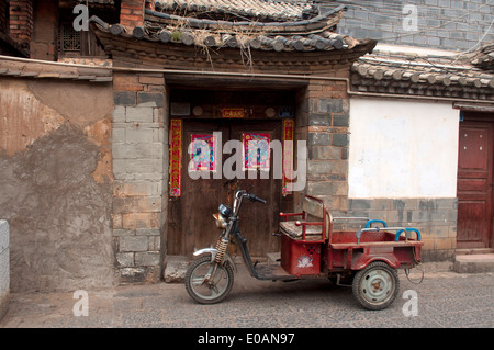 Ein elektrisches Dreirad steht vor einer traditionellen Eingangstür in Jianshui, Yunnan, China Stockfoto