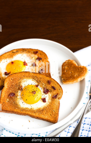 Ei in einen Toast herzförmigen Ausschnitt gebraten mit Speck Krümel, Pfeffer und Thymian bestreut Stockfoto