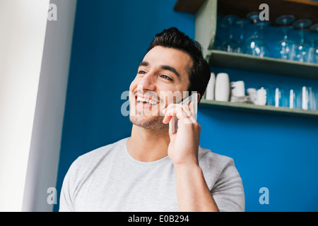 Porträt des Lachens jungen Mannes telefonieren mit Smartphone in seiner Küche Stockfoto