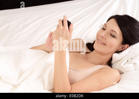 Frau liegt im Bett und las eine Sms auf ihr Handy Stockfoto