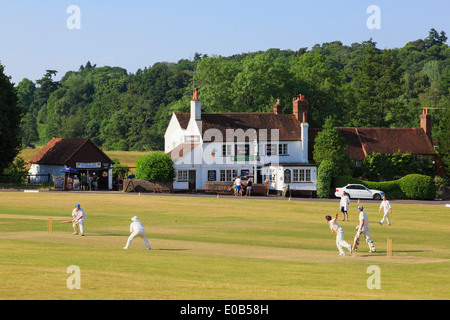 Lokale Landmannschaften spielen an einem Sommerabend ein Cricket-Spiel auf einem Dorfgrün vor dem Barley Mow Pub. Tilford Surrey England, Großbritannien Stockfoto