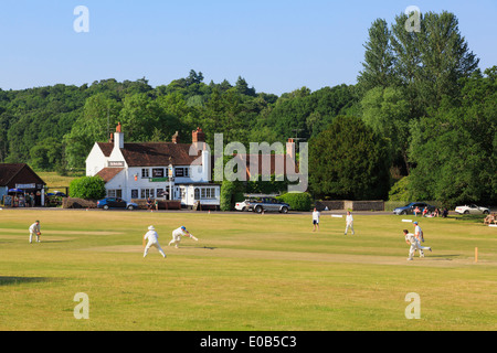 Lokale Teams spielen ein Cricket Spiel am Dorfanger vor Gerste Mähen Pub an einem Sommerabend. Tilford Surrey England UK Stockfoto