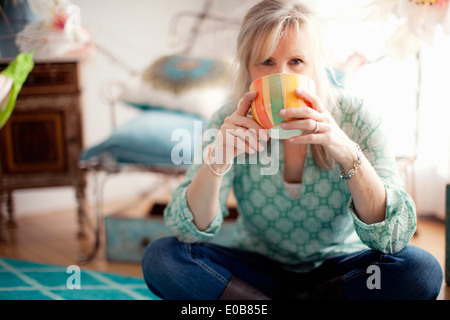 Reife Frau sitzen cross legged Kaffeetrinken Stockfoto