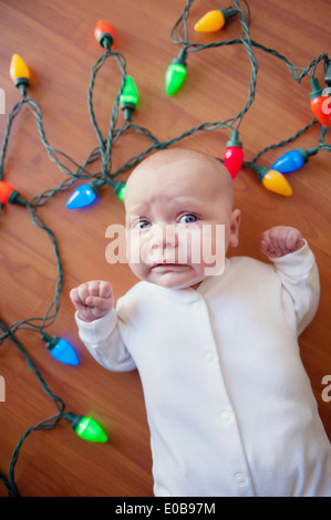 Baby auf Boden umgeben von Weihnachtsbeleuchtung Stockfoto