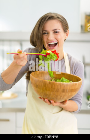 Porträt der glückliche junge Hausfrau Verkostung Salat in Küche Stockfoto