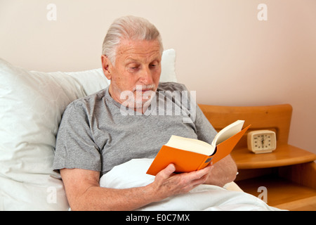 ein Boss im Altersheim mit dem Buch lesen im Bett, Ein Senior Im Altenheim Beim Buch Lesen Im Bett Stockfoto