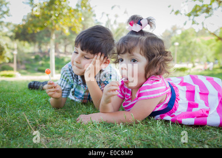 Cute Young Bruder und kleine Schwester ihren Lutscher im Freien auf dem Rasen genießen. Stockfoto