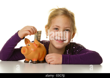 Ein kleines Kind stellt eine Banknote in ein Sparschwein. Dollar, Ein Kleines Kind Steckt Einen Geldschein in Ein Sparschwein. Dollar. Stockfoto