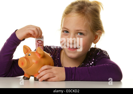 Ein kleines Kind stellt eine Banknote in ein Sparschwein Stockfoto