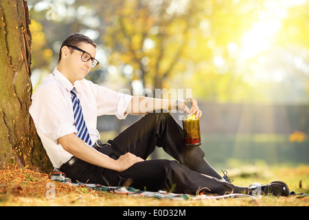 Enttäuscht junger Geschäftsmann sitzen auf einem Rasen mit Flasche in der Hand, im park Stockfoto