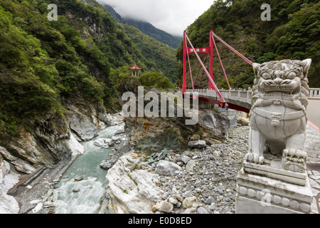 Marmor Löwenstatue vor einer roten Cimu/Cihmu-Brücke und dazwischen üppige & steile Berge im Taroko National Park im Taiw Stockfoto