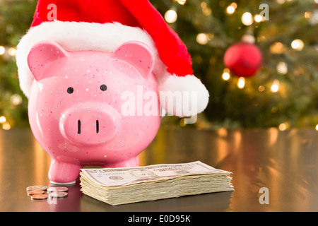 Sparschwein mit Santa Claus Hut mit Währung auf Tisch platziert. Stockfoto