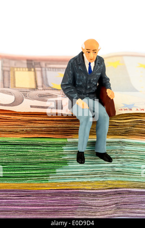 Symbolische Foto für den Ruhestand und die Altersvorsorge, Figur eines alten Mannes sitzt auf einem Haufen von Banknoten, Symbolfoto für Stockfoto