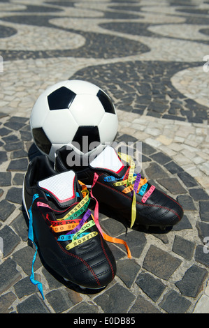 Viel Glück Fußballschuhe Stollen geschnürt mit brasilianischen Wunsch Bändern am Copacabana-Strand Gehweg mit Fußball Ball Rio De Janeiro Stockfoto