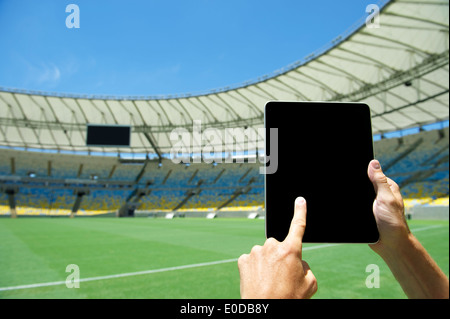Finger berühren leere Tablet Computerbildschirm vor Fußballplatz im Fußballstadion Rio De Janeiro Brasilien Stockfoto