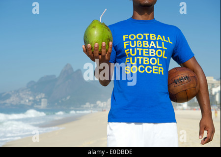 Brasilianische Fußballspieler in Multi Sprache Nachricht Shirt Vintage Fußball halten und trinken Coco Verde Kokosnuss Rio De Janeiro Stockfoto